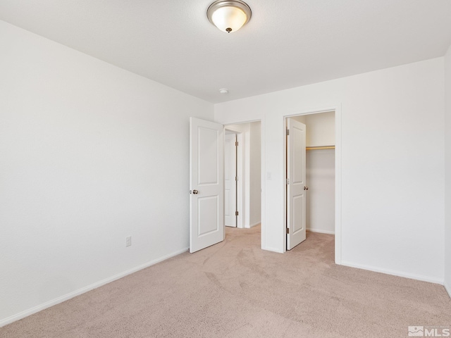 unfurnished bedroom with baseboards, a walk in closet, a closet, and light colored carpet