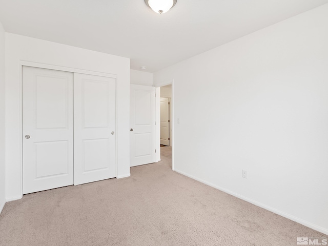 unfurnished bedroom featuring a closet, light colored carpet, and baseboards