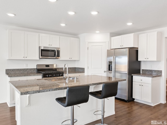 kitchen with appliances with stainless steel finishes, dark wood-style flooring, a center island with sink, and white cabinetry