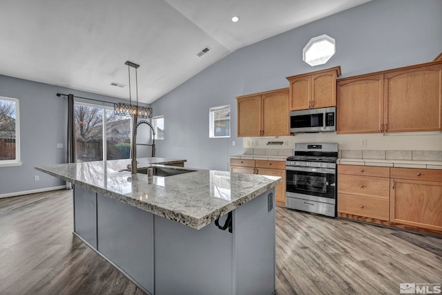 kitchen featuring an island with sink, stainless steel appliances, a sink, and hanging light fixtures