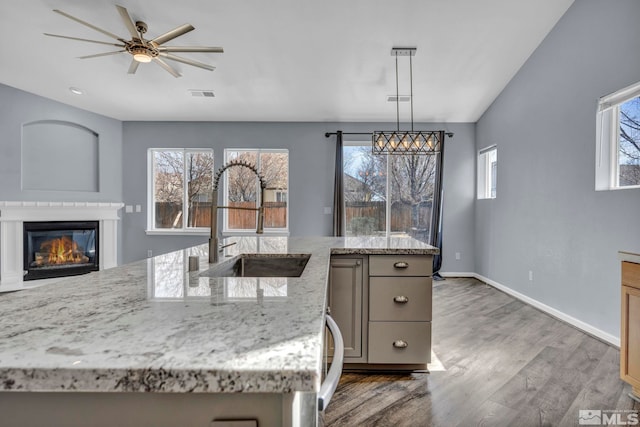 kitchen with light stone counters, decorative light fixtures, a glass covered fireplace, a sink, and wood finished floors