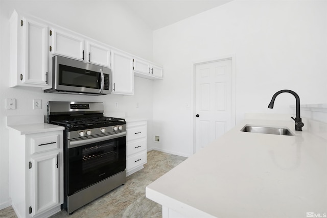 kitchen featuring appliances with stainless steel finishes, white cabinets, light countertops, and a sink