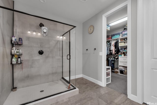 bathroom with baseboards, a spacious closet, and a shower stall