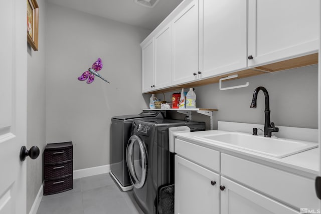 laundry area featuring light tile patterned floors, a sink, baseboards, washer and dryer, and cabinet space