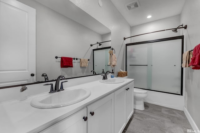 bathroom with double vanity, shower / bath combination with glass door, a sink, and visible vents