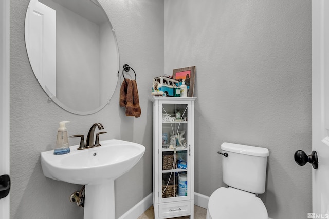 bathroom with a textured wall, baseboards, a sink, and toilet