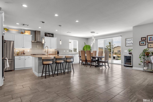 kitchen featuring wall chimney range hood, a kitchen island with sink, light countertops, and decorative light fixtures