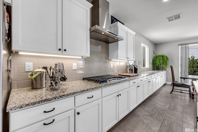 kitchen featuring light stone counters, stainless steel gas cooktop, visible vents, white cabinets, and wall chimney exhaust hood