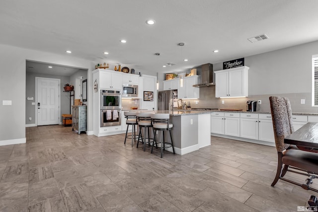 kitchen with a center island, a breakfast bar, stainless steel appliances, visible vents, and wall chimney exhaust hood