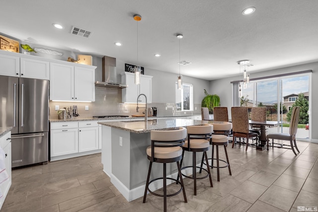 kitchen with visible vents, a center island with sink, high end refrigerator, and wall chimney exhaust hood