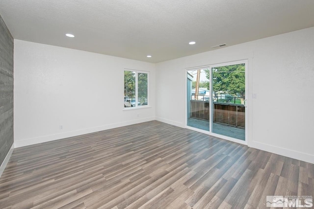 unfurnished room with baseboards, a textured ceiling, visible vents, and wood finished floors