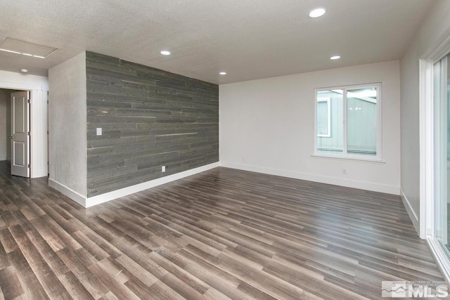 spare room featuring wood walls, an accent wall, dark wood finished floors, and a textured ceiling