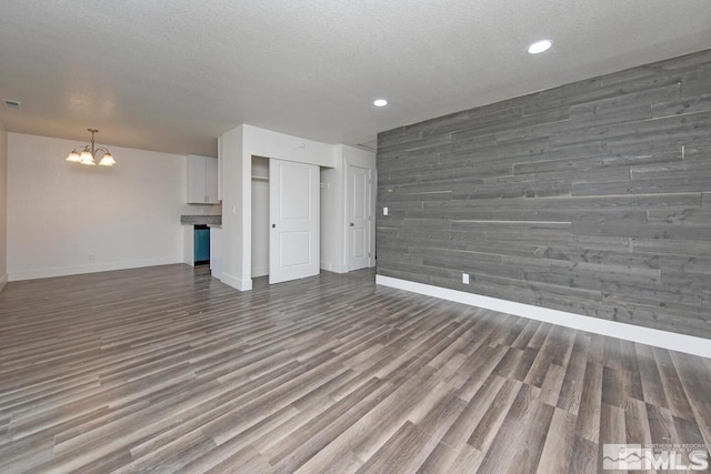 unfurnished living room with wooden walls, baseboards, dark wood finished floors, a textured ceiling, and a notable chandelier