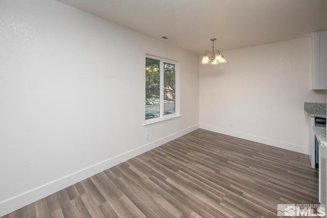 unfurnished dining area with a chandelier, dark wood-type flooring, visible vents, and baseboards