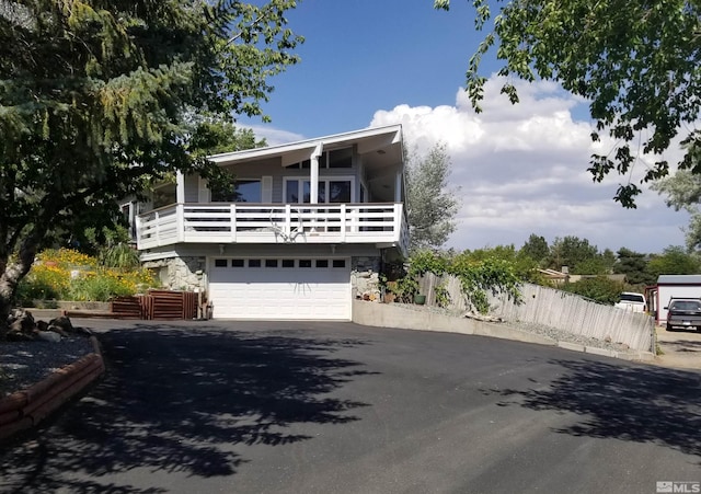 view of front of home featuring aphalt driveway, an attached garage, a balcony, fence, and stone siding