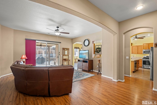 living area with light wood-type flooring, arched walkways, ceiling fan, and baseboards