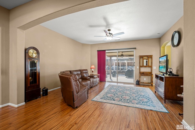 living area featuring a ceiling fan, baseboards, arched walkways, and wood finished floors