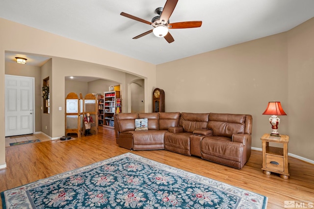 living area featuring a ceiling fan, baseboards, arched walkways, and wood finished floors