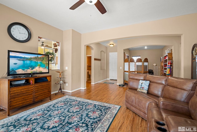 living area featuring light wood-style floors, arched walkways, baseboards, and a ceiling fan