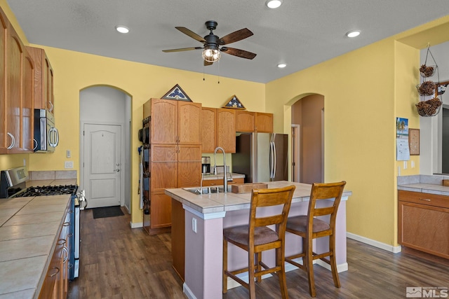 kitchen featuring arched walkways, tile countertops, appliances with stainless steel finishes, and a center island