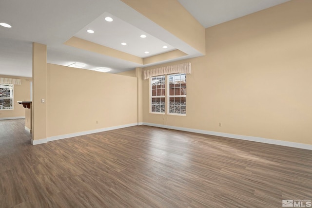 spare room featuring dark wood-style floors, a tray ceiling, and baseboards