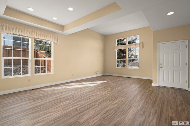 spare room featuring wood finished floors, recessed lighting, a raised ceiling, and baseboards