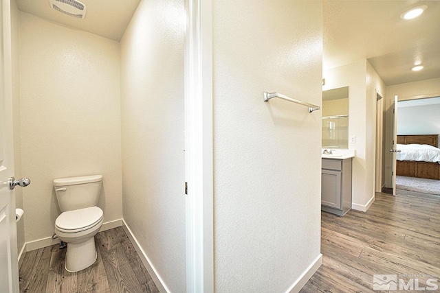 ensuite bathroom with connected bathroom, toilet, wood finished floors, visible vents, and baseboards