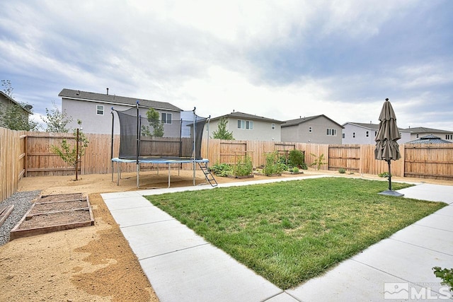 view of yard featuring a trampoline, a residential view, a fenced backyard, and a vegetable garden