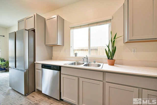 kitchen featuring stainless steel appliances, light countertops, a sink, and light wood-style flooring