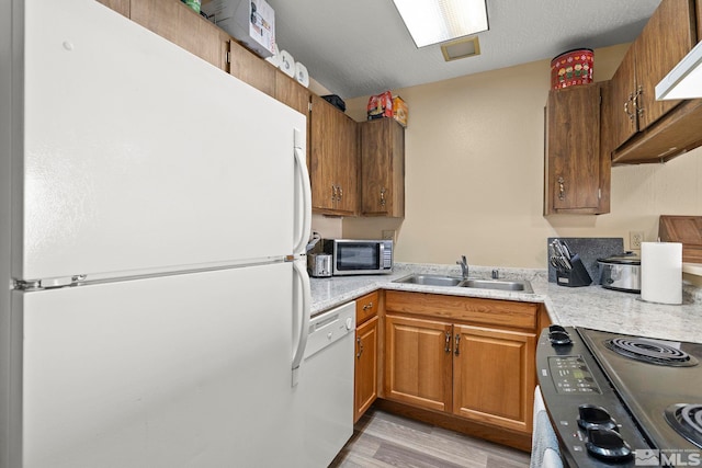 kitchen with white appliances, a sink, light wood-style floors, light countertops, and brown cabinets