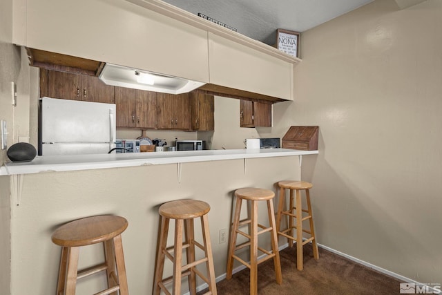 kitchen with a breakfast bar, light countertops, dark carpet, freestanding refrigerator, and a peninsula