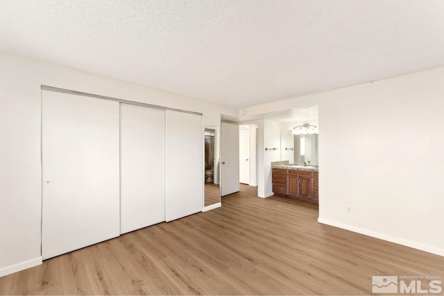 unfurnished bedroom featuring baseboards, light wood-style flooring, ensuite bathroom, a textured ceiling, and a closet