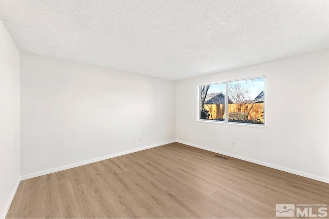 unfurnished room featuring a textured ceiling, light wood-type flooring, visible vents, and baseboards