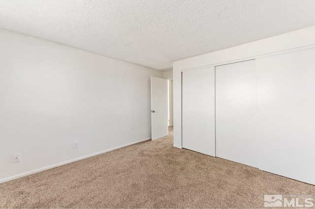 unfurnished bedroom featuring a closet, light carpet, a textured ceiling, and baseboards