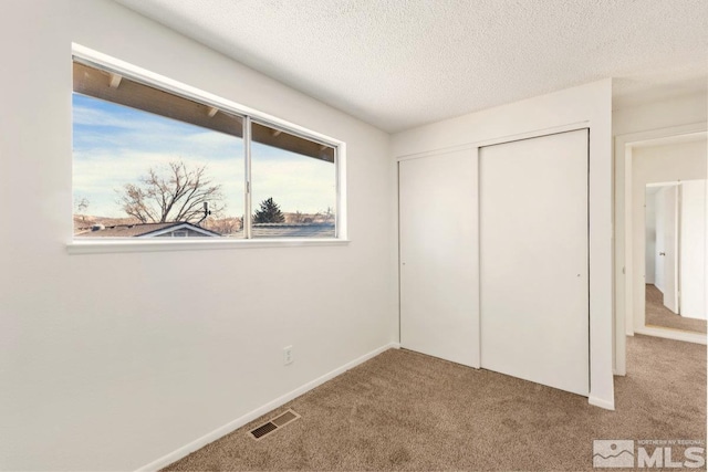 unfurnished bedroom with a closet, visible vents, carpet flooring, a textured ceiling, and baseboards