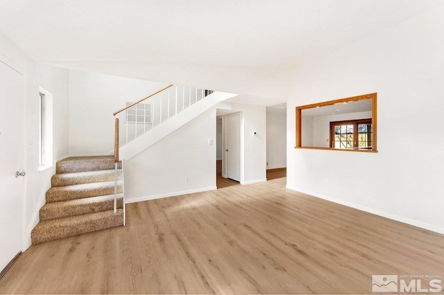 unfurnished living room featuring light wood-style floors, baseboards, and stairway