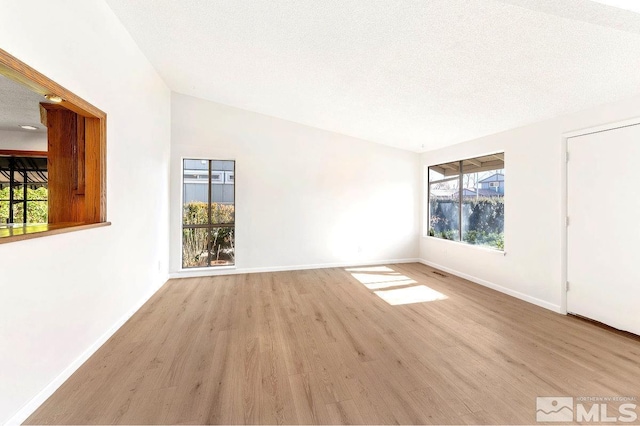 spare room featuring a textured ceiling, light wood finished floors, visible vents, and baseboards