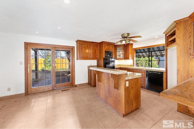 kitchen with a kitchen breakfast bar, a center island, black appliances, brown cabinetry, and plenty of natural light