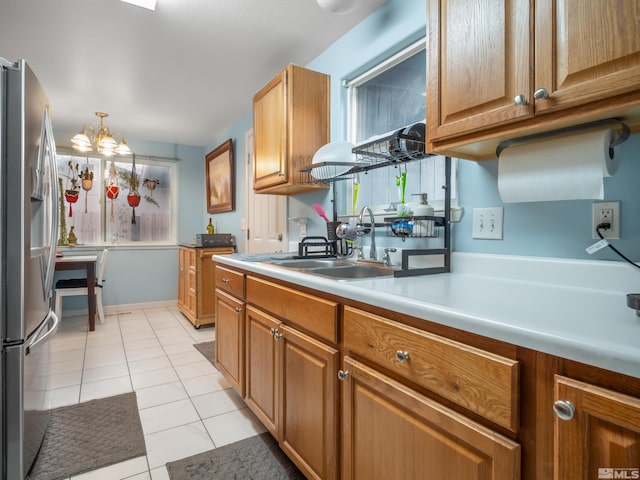 kitchen featuring decorative light fixtures, stainless steel refrigerator with ice dispenser, light countertops, brown cabinetry, and a sink