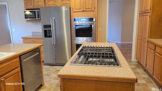 kitchen with light countertops, appliances with stainless steel finishes, brown cabinetry, and a kitchen island