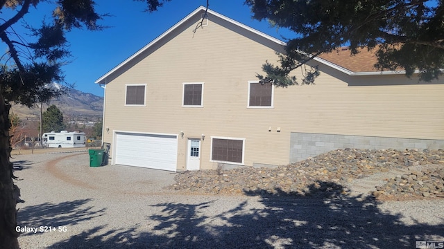 view of property exterior with a garage, gravel driveway, and a mountain view