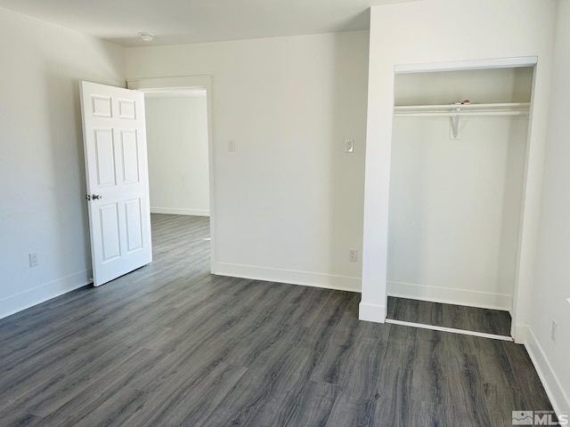 unfurnished bedroom with a closet, baseboards, and dark wood-type flooring