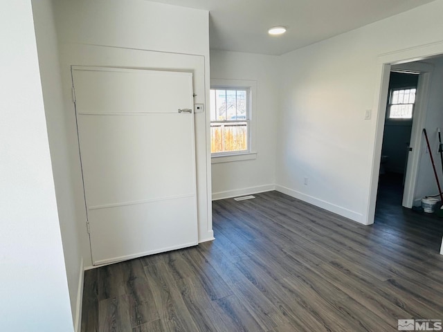 unfurnished bedroom with multiple windows, dark wood finished floors, and baseboards