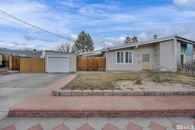 mid-century modern home with driveway, a detached garage, and fence