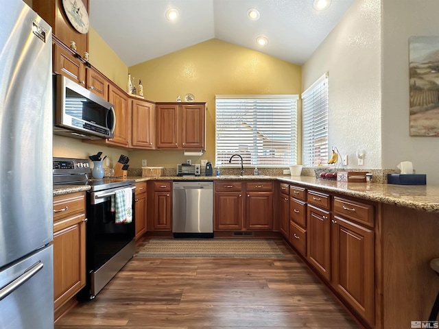 kitchen featuring dark wood-style floors, appliances with stainless steel finishes, brown cabinets, vaulted ceiling, and a sink