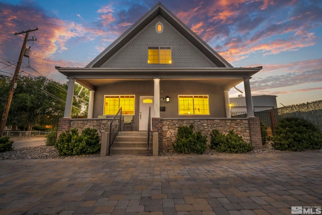 view of front of home featuring covered porch, stone siding, and stucco siding