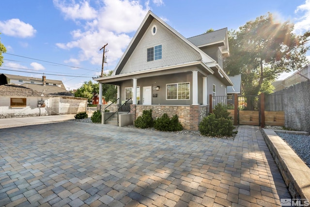 view of front facade featuring stucco siding, a porch, a gate, fence, and stone siding