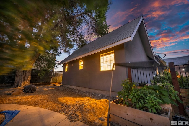 property exterior at dusk with a garden, fence, and stucco siding