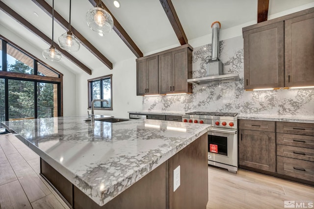 kitchen featuring wall chimney range hood, premium range, light stone counters, and an island with sink