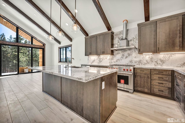 kitchen featuring light stone counters, a sink, wall chimney range hood, designer range, and an island with sink